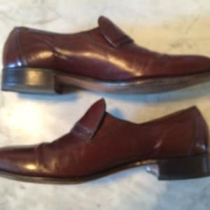 May include: A pair of brown leather slip-on shoes with a pointed toe. The shoes have a simple design and are made of high-quality leather.