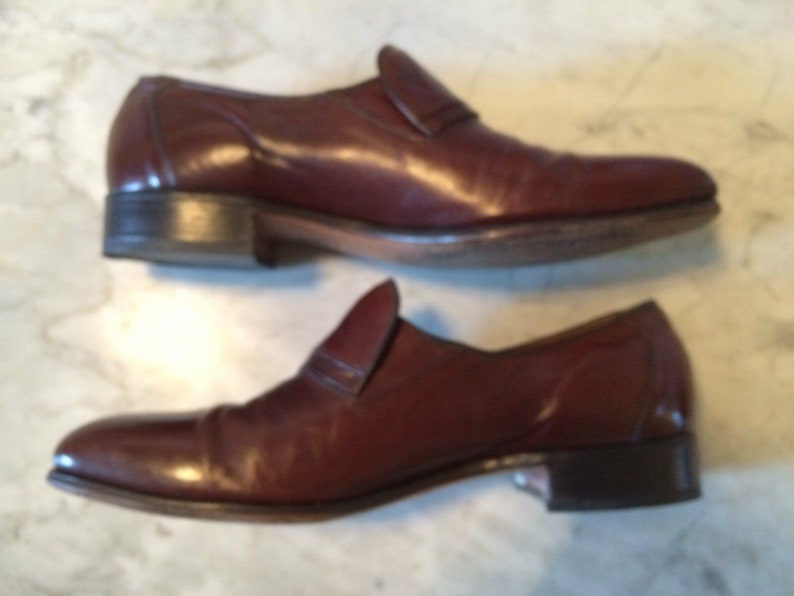 May include: A pair of brown leather slip-on shoes with a pointed toe. The shoes have a simple design and are made of high-quality leather.