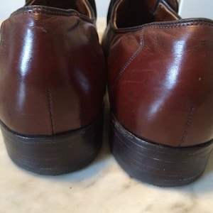 May include: A pair of brown leather loafers with black soles. The shoes have a polished finish and are slightly scuffed.