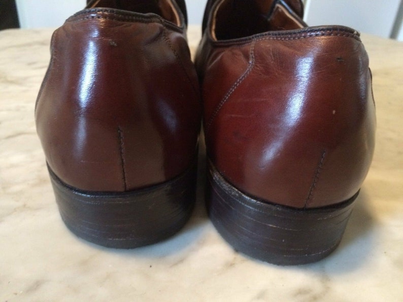 May include: A pair of brown leather loafers with black soles. The shoes have a polished finish and are slightly scuffed.