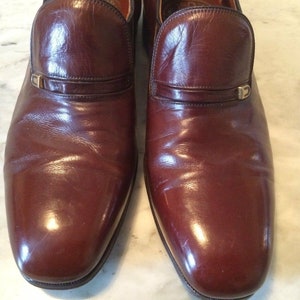 May include: A pair of brown leather slip-on shoes with a gold buckle detail.