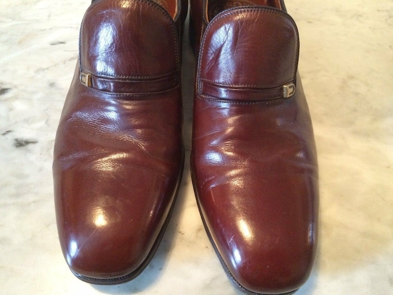 May include: A pair of brown leather slip-on shoes with a gold buckle detail.