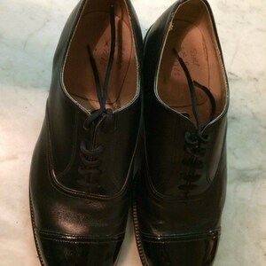 May include: A pair of black leather lace-up shoes with a cap toe. The shoes have a polished finish and are marked "Size 7 1/2" and "Size 7 1/2" on the inside.