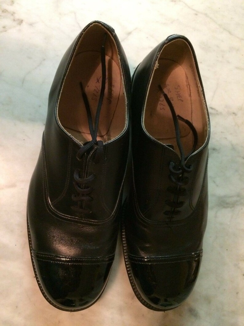 May include: A pair of black leather lace-up shoes with a cap toe. The shoes have a polished finish and are marked "Size 7 1/2" and "Size 7 1/2" on the inside.