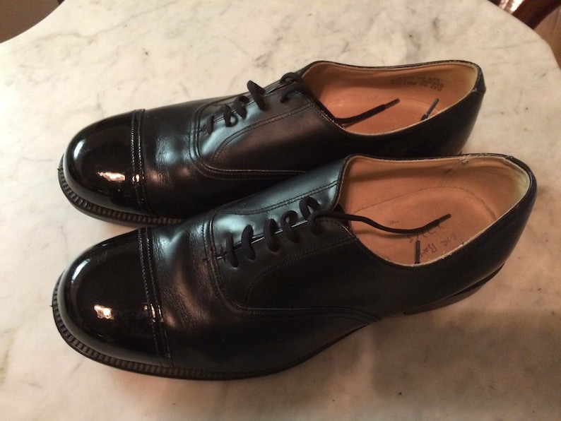 May include: A pair of black leather lace-up shoes with a cap toe. The shoes have a polished finish and a slightly rounded toe.