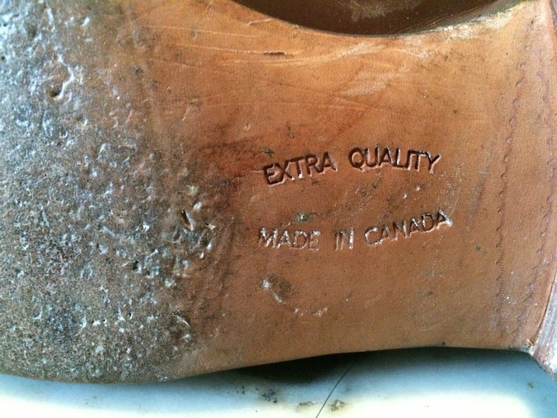 May include: Close-up of the bottom of a brown leather shoe with the text "EXTRA QUALITY MADE IN CANADA" embossed on the sole.
