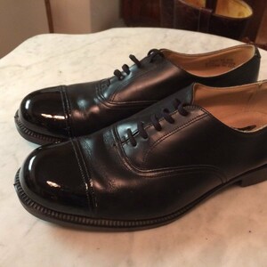 May include: A pair of black leather lace-up shoes with a cap toe. The cap toe is shiny and black.