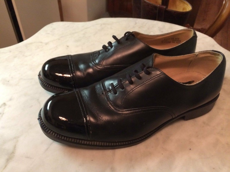 May include: A pair of black leather lace-up shoes with a cap toe. The cap toe is shiny and black.