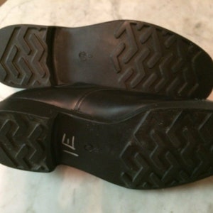 May include: Close-up of the black leather soles of a pair of dress shoes. The soles have a textured pattern and the text "IE" is visible on one sole.
