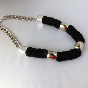 May include: A black rope necklace with silver metal accents. The necklace has a chain link fastening.