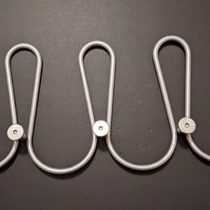 May include: A silver metal coat rack with three hooks. The hooks are shaped like a U and have a round knob at the end.