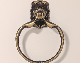 May include: An antique-style towel ring with a decorative backplate and a circular ring. The metal fixture has a bronze finish with ornate detailing. The ring is designed to hold a towel and is mounted on a wall.