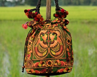 May include: A colorful embroidered drawstring bag with black handles and pom-poms. The bag is decorated with intricate floral and bird patterns in shades of orange, yellow, green, and red.