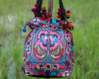 May include: A black tote bag with colorful embroidered flowers and birds. The bag has a drawstring closure and is decorated with colorful pom-poms.