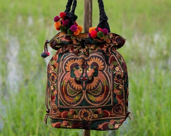 May include: A black and green embroidered tote bag with colorful pom-poms. The bag features a floral design with two birds.