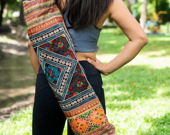 May include: A woman carrying a colorful yoga mat bag with intricate embroidery. The bag is made of fabric and has a black background with colorful geometric patterns.