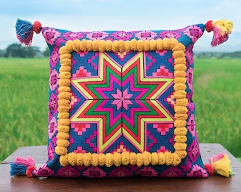 May include: A pink and blue throw pillow with a yellow pom-pom trim and a colorful starburst design in the center.