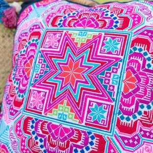 May include: A colorful throw pillow with a geometric pattern featuring a large star in the center. The pillow is made of a soft, woven fabric and has a white background with pink, blue, green, and red accents.