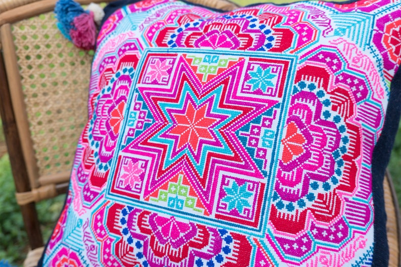 May include: A colorful throw pillow with a geometric pattern featuring a large star in the center. The pillow is made of a soft, woven fabric and has a white background with pink, blue, green, and red accents.