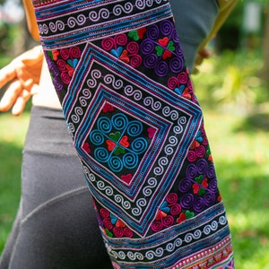 May include: A colorful yoga mat with intricate embroidery featuring geometric patterns and swirls in shades of pink, blue, green, and purple on a black background.