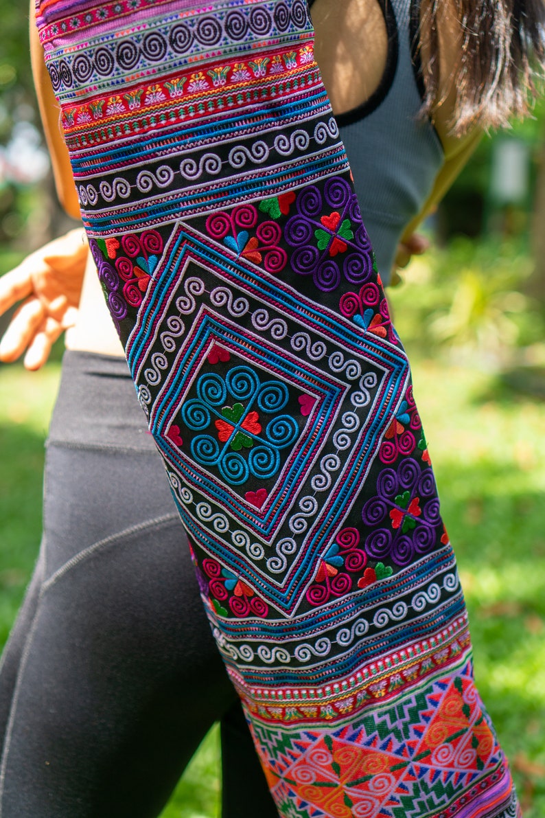 May include: A colorful yoga mat with intricate embroidery featuring geometric patterns and swirls in shades of pink, blue, green, and purple on a black background.