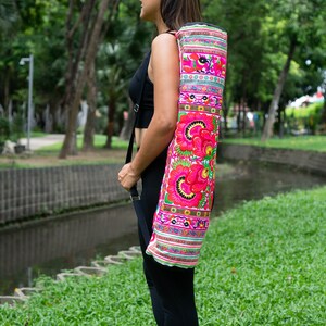 Puede incluir: Una mujer con leggings negros lleva una bolsa de esterilla de yoga blanca con flores y patrones bordados de colores.