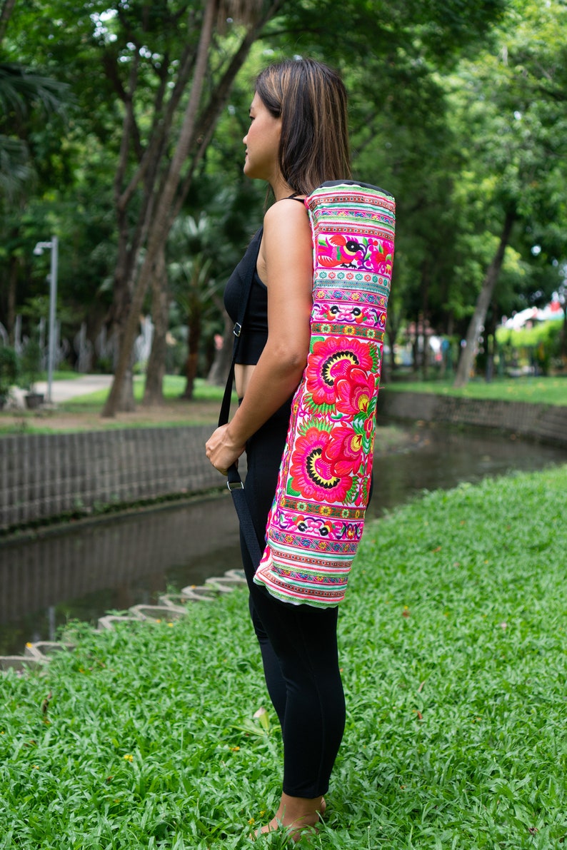 Puede incluir: Una mujer con leggings negros lleva una bolsa de esterilla de yoga blanca con flores y patrones bordados de colores.