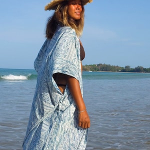 Pode incluir: Uma mulher vestindo um quimono azul e branco com um chapéu de palha em uma praia.