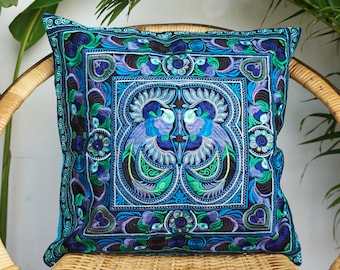 May include: A blue and green embroidered throw pillow with a floral pattern and two birds in the center.