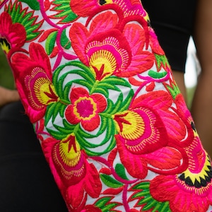 Puede incluir: Un coj&iacute;n de yoga blanco con un dise&ntilde;o de bordado floral colorido. El bordado presenta flores rosas, rojas, amarillas y verdes.