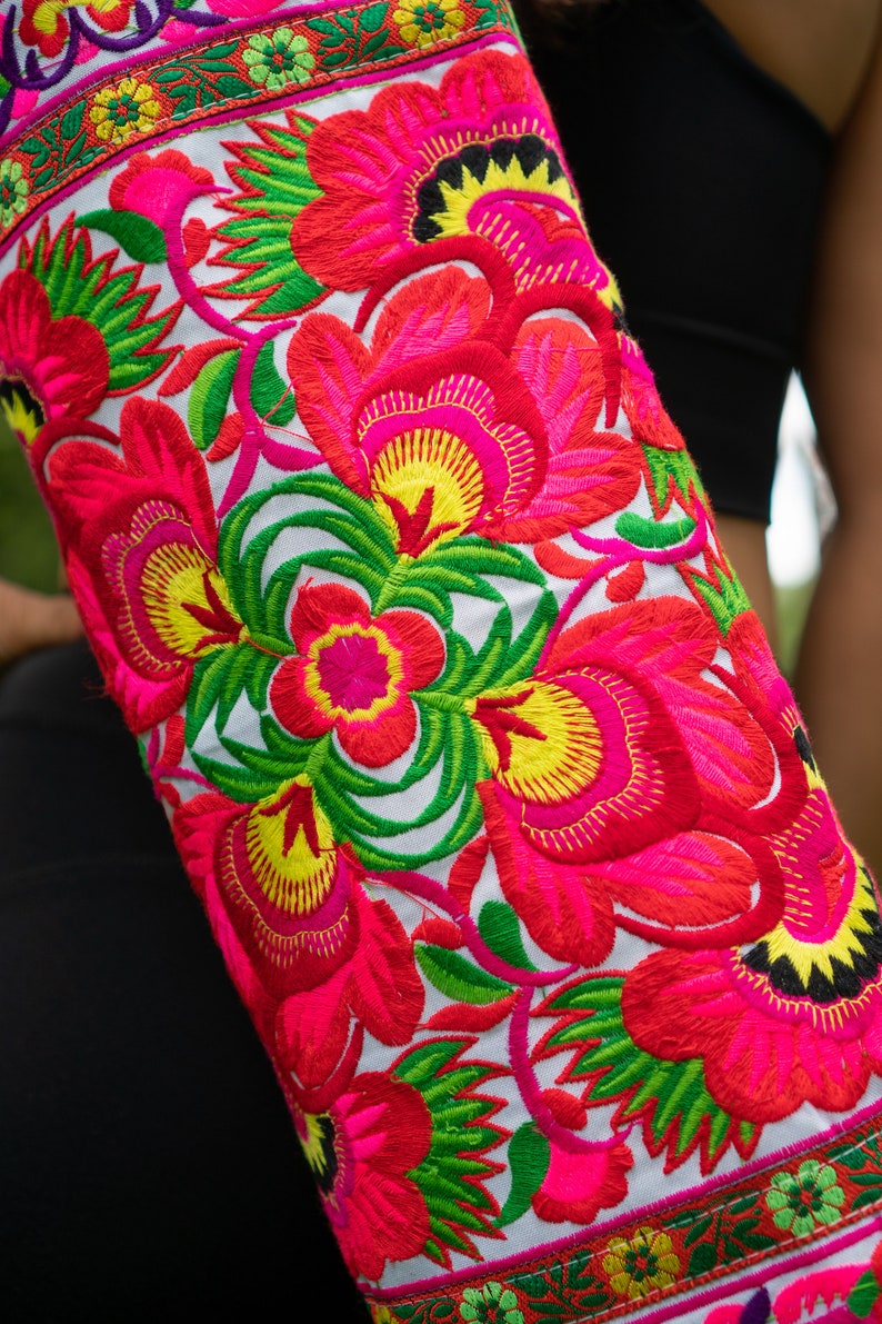Puede incluir: Un coj&iacute;n de yoga blanco con un dise&ntilde;o de bordado floral colorido. El bordado presenta flores rosas, rojas, amarillas y verdes.
