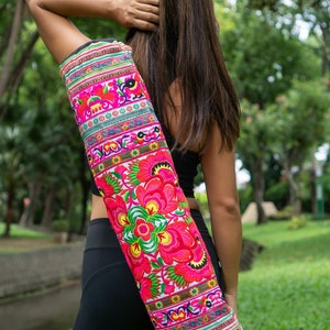 Puede incluir: Una mujer llevando una bolsa de yoga con un estampado floral colorido. La bolsa est&aacute; hecha de tela y tiene una correa que se coloca sobre el hombro. La bolsa est&aacute; decorada con flores rosas, rojas, verdes y amarillas.