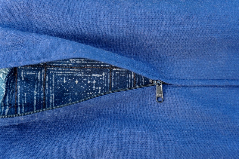 May include: A blue zippered pillow cover with a white and blue patterned fabric lining. The zipper pull is silver.