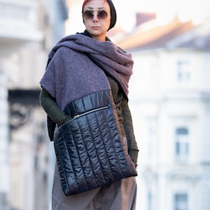 May include: A person wearing a gray and purple scarf, a black quilted bag, gray pants, and burgundy boots. The person is standing on a brick walkway.