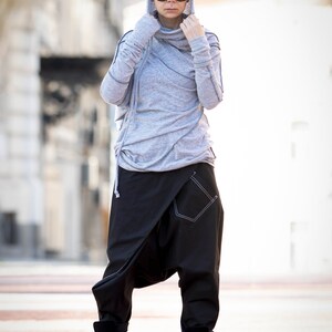 May include: A woman wearing a gray hooded sweater with a black and white patterned design and black pants. She is wearing black boots and sunglasses.