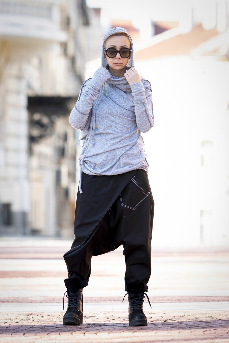 May include: A woman wearing a gray hooded sweater with a black and white patterned design and black pants. She is wearing black boots and sunglasses.