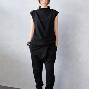 May include: A black ensemble featuring a mock neck top and drop-crotch pants. The top has short sleeves, and the pants have a unique draped design. The outfit is paired with black boots and a black bracelet. The clothing is made of a smooth fabric.