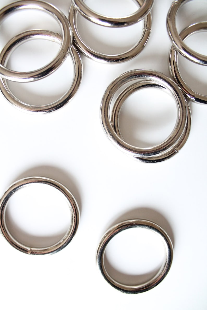 Puede incluir: Un grupo de anillos de metal plateado, algunos apilados uno encima del otro, sobre un fondo blanco.