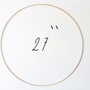 May include: A gold metal hoop with a diameter of 27 inches. The hoop is hanging on a white wall.