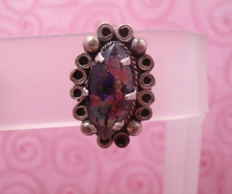 May include: A silver ring with a marbled iridescent glass stone set in a decorative silver bezel.