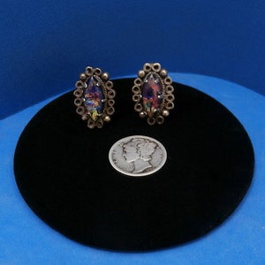 May include: A pair of silver earrings with iridescent stones set in a circular design. The earrings are about the size of a dime.