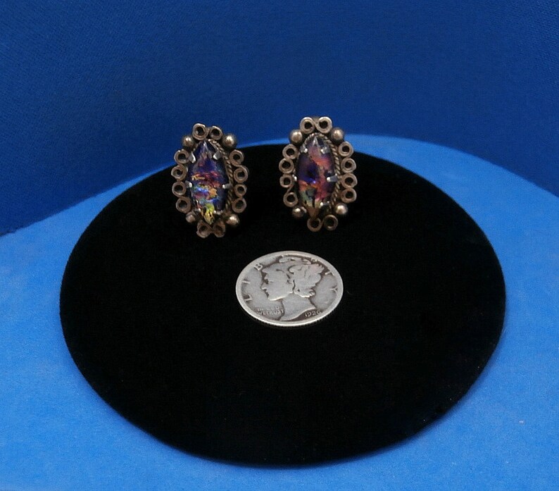 May include: A pair of silver earrings with iridescent stones set in a circular design. The earrings are about the size of a dime.