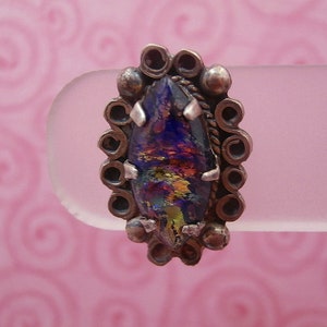 May include: A silver ring with a large, iridescent, multi-colored glass stone set in a decorative, ornate silver setting.