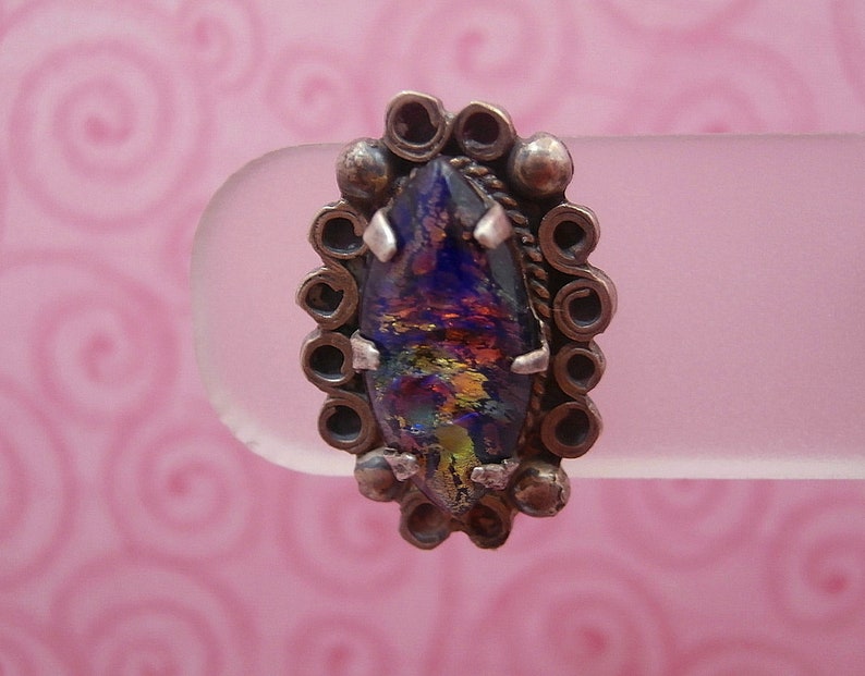 May include: A silver ring with a large, iridescent, multi-colored glass stone set in a decorative, ornate silver setting.