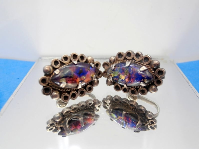 May include: A pair of silver earrings with a colorful opal stone set in a decorative silver frame.