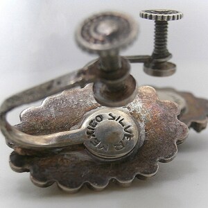 May include: Silver tone earrings with a floral design and a screw back closure. The earrings are marked "T.I.G.O. SILVER".