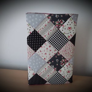 May include: A patchwork book cover with a variety of fabrics in black, white, grey, and pink. The cover features polka dots, floral prints, and gingham checks. The rectangular cover appears to be handmade, with a quilted design.