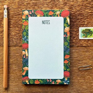 May include: A notepad with a green background and a white border. The border is decorated with mushrooms, leaves, and vines. The notepad has the word "NOTES" printed at the top.