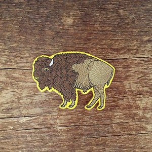 K&ouml;nnte beinhalten: Ein braunes gesticktes Patch mit einem Bison mit gelber Umrandung. Der Bison blickt nach links und hat ein wei&szlig;es Horn.