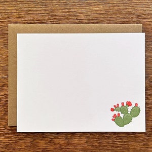 May include: A blank white card with a brown envelope and a cactus illustration. The card has a red and green cactus with red flowers. A postage stamp with a bird on it is in the upper right corner.